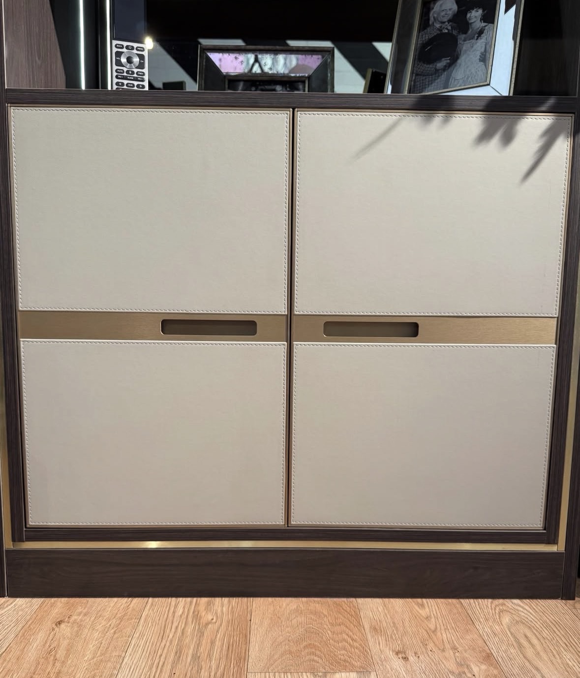 Close detail of stitched cream leather cabinet doors with a brushed brass recessed handle rail on dark oak cabinetry