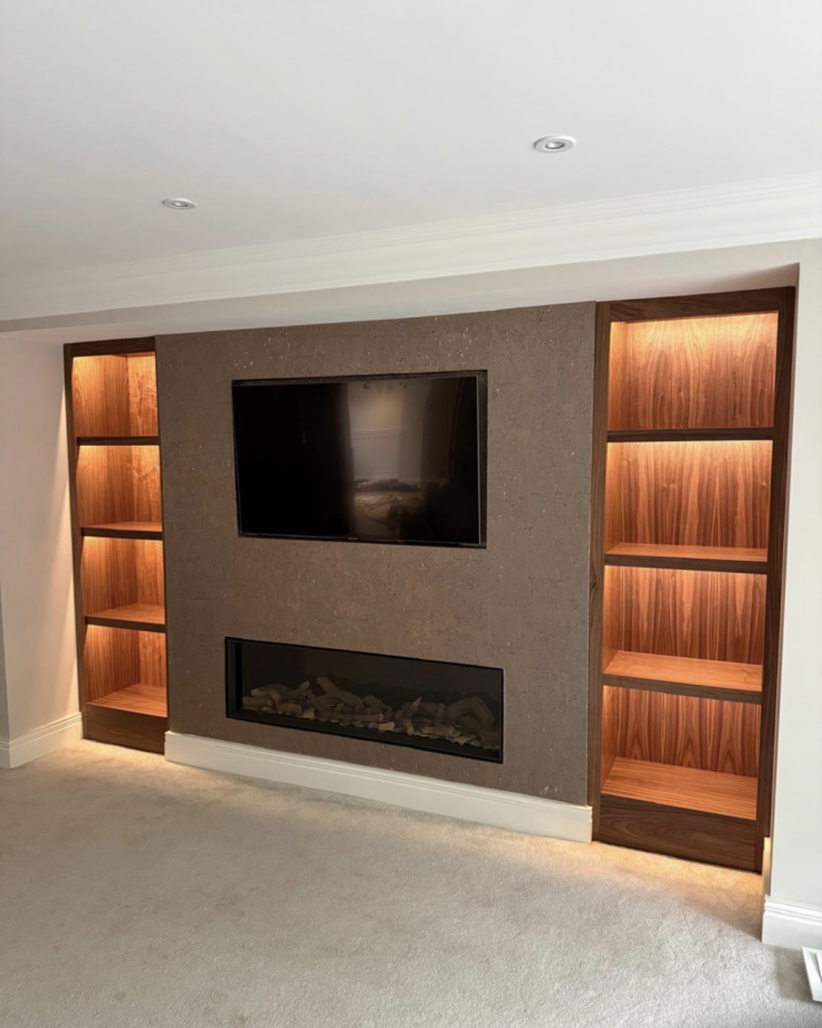 Matching LED-lit timber alcove shelving either side of a chimney breast with a recessed television and inset fire