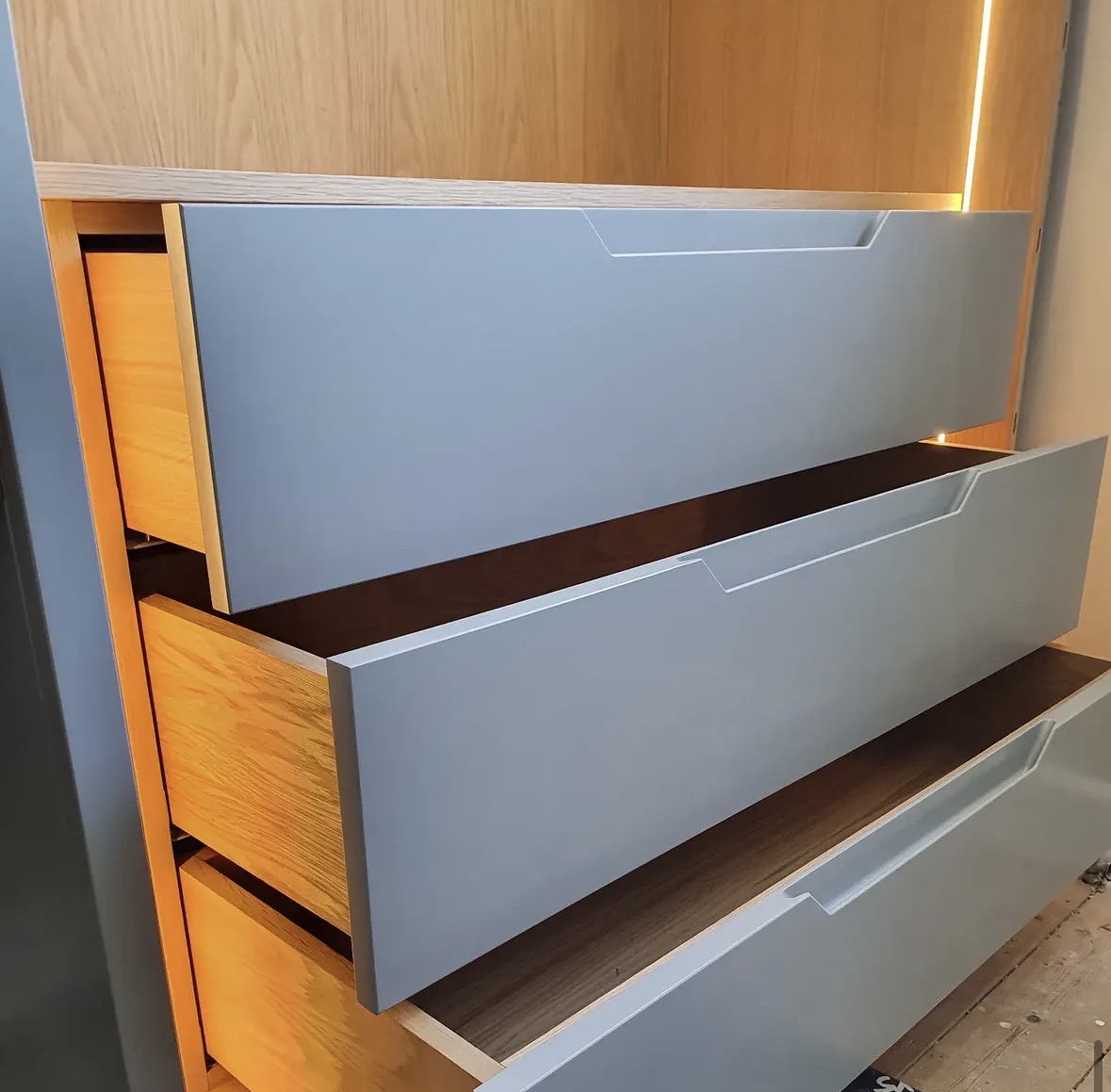 Detail of handleless painted drawers with solid oak interiors and a warm LED-lit oak cabinet above