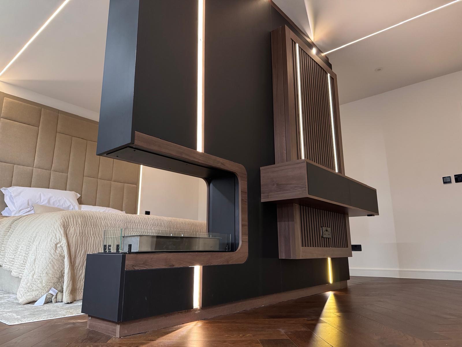 Angled view of a black and walnut bedroom media wall with slatted walnut panelling, floating cabinets and integrated LED strips