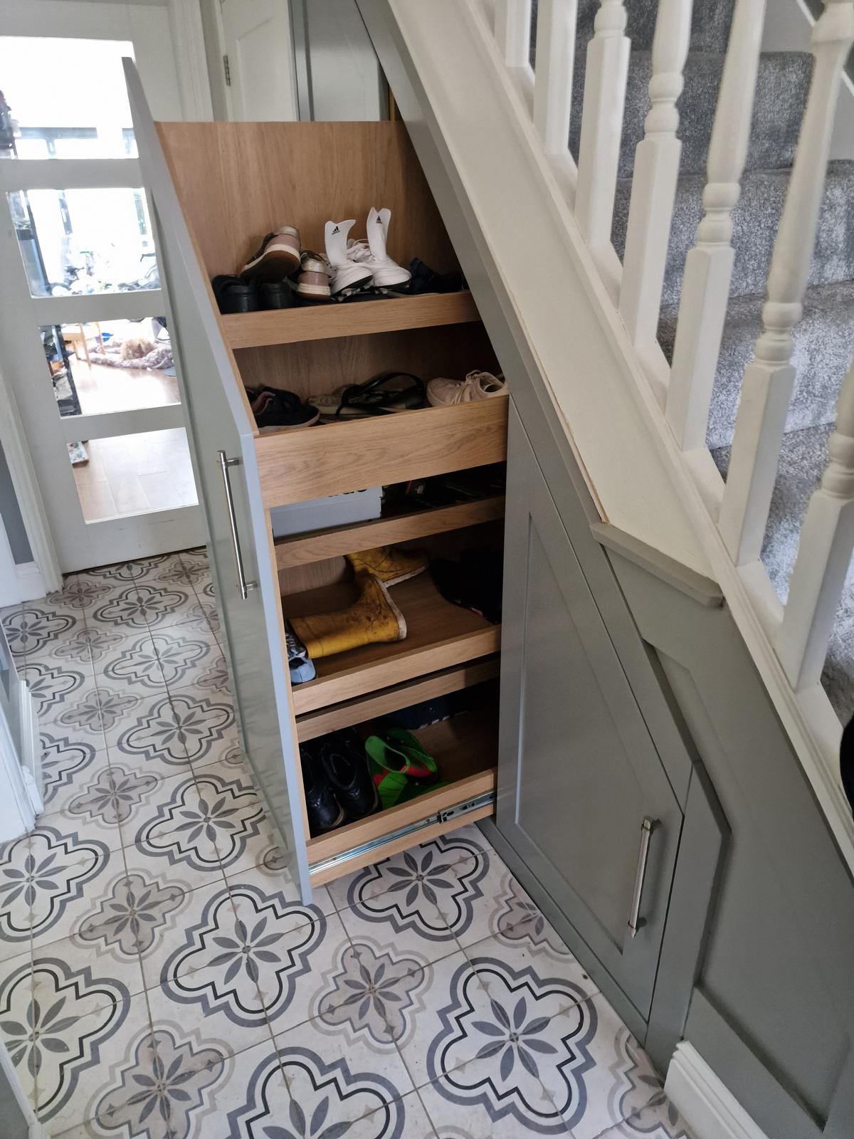 Painted under-stairs cupboard opened to show oak pull-out shoe trays following the rake of the staircase
