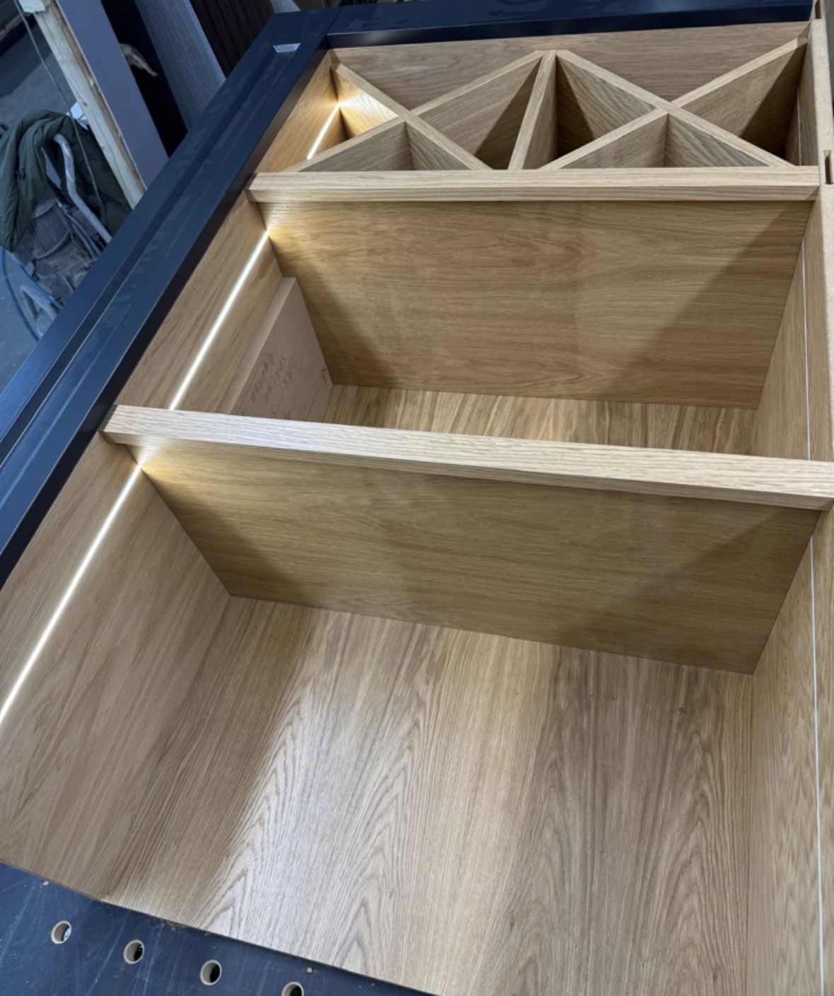 Cross-hatch oak wine racking and LED-lit oak shelving being fitted into a navy painted drinks unit