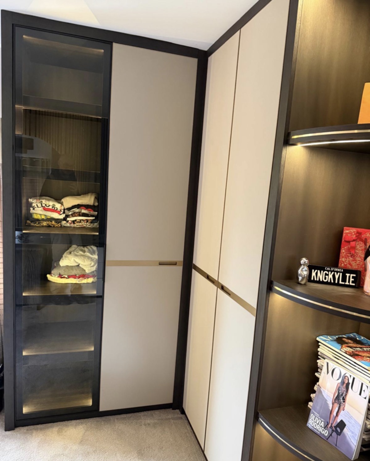 Fitted wardrobes in cream and bronze with smoked glass display doors and a curved corner shelf run