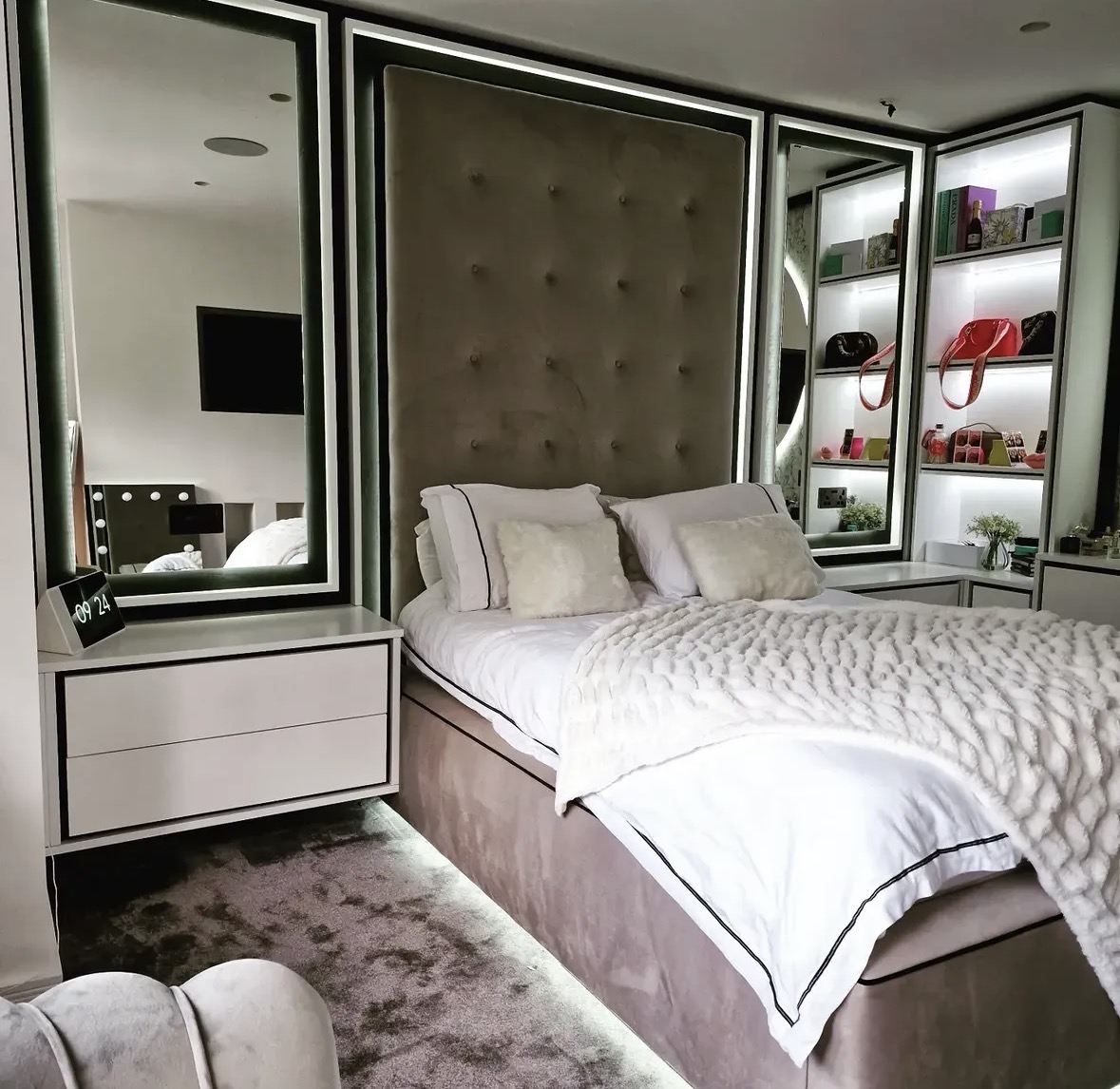 Bespoke bedroom wall with buttoned upholstered headboard panels, backlit mirrors and illuminated display shelving