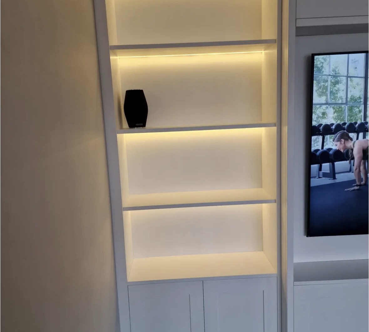 Close detail of warm-lit display shelving in an ivory shaker-style fitted media wall