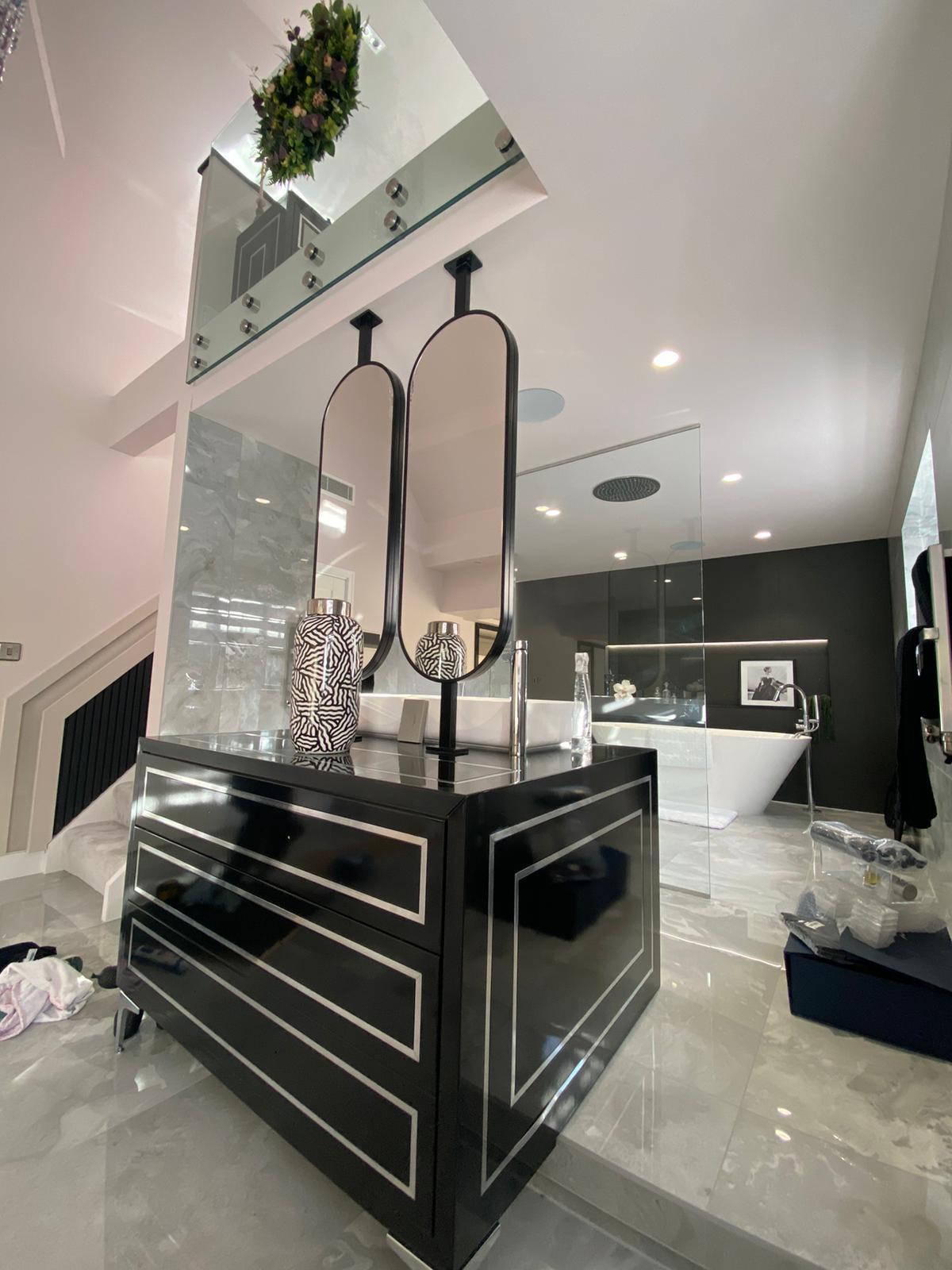 High-gloss black bathroom vanity island with chrome inlay detailing and twin suspended mirrors in a marble-tiled bathroom