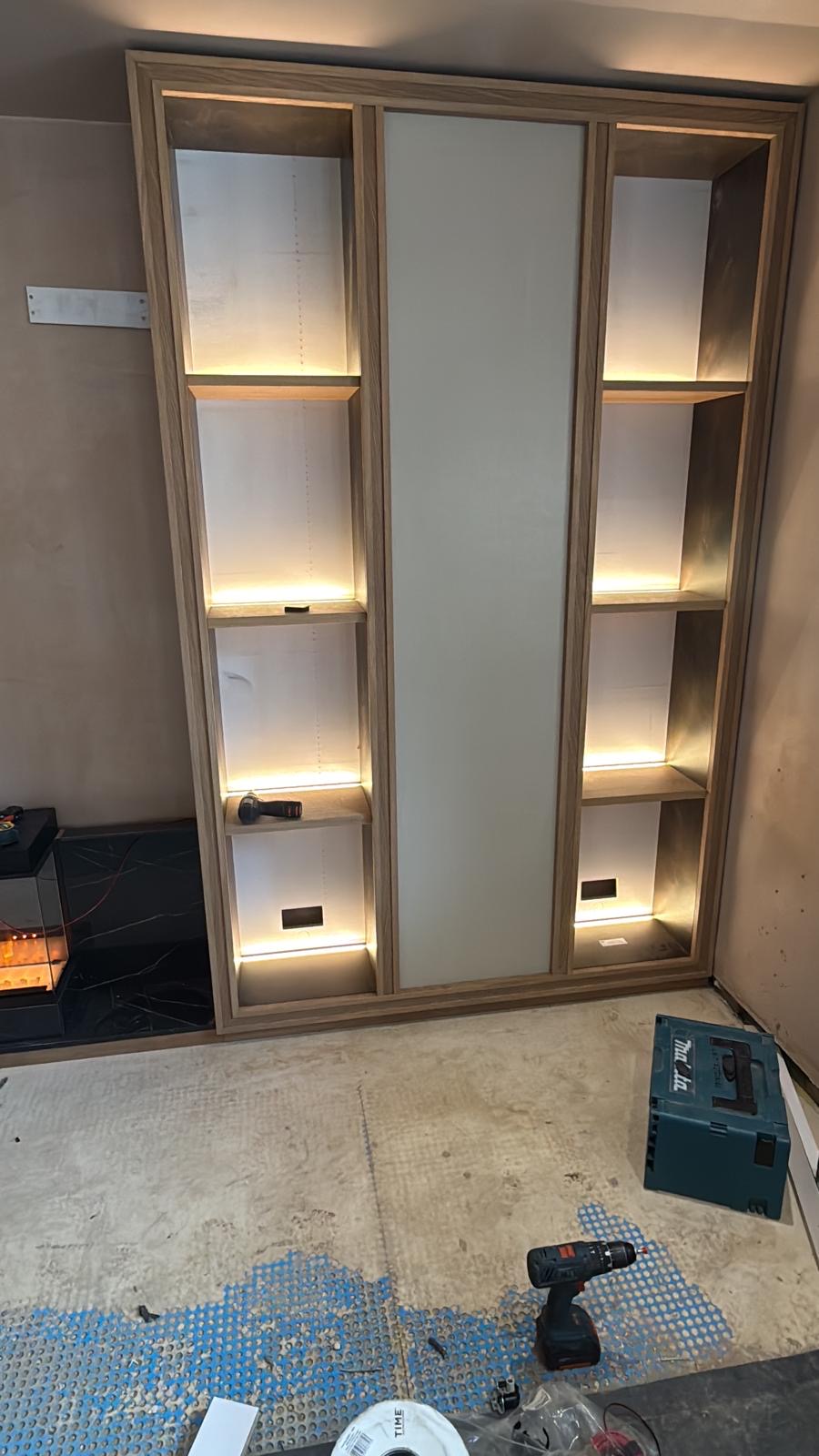 Oak display shelving with integrated LED lighting during installation of the Solihull bespoke media wall, before the marble centrepiece was fitted