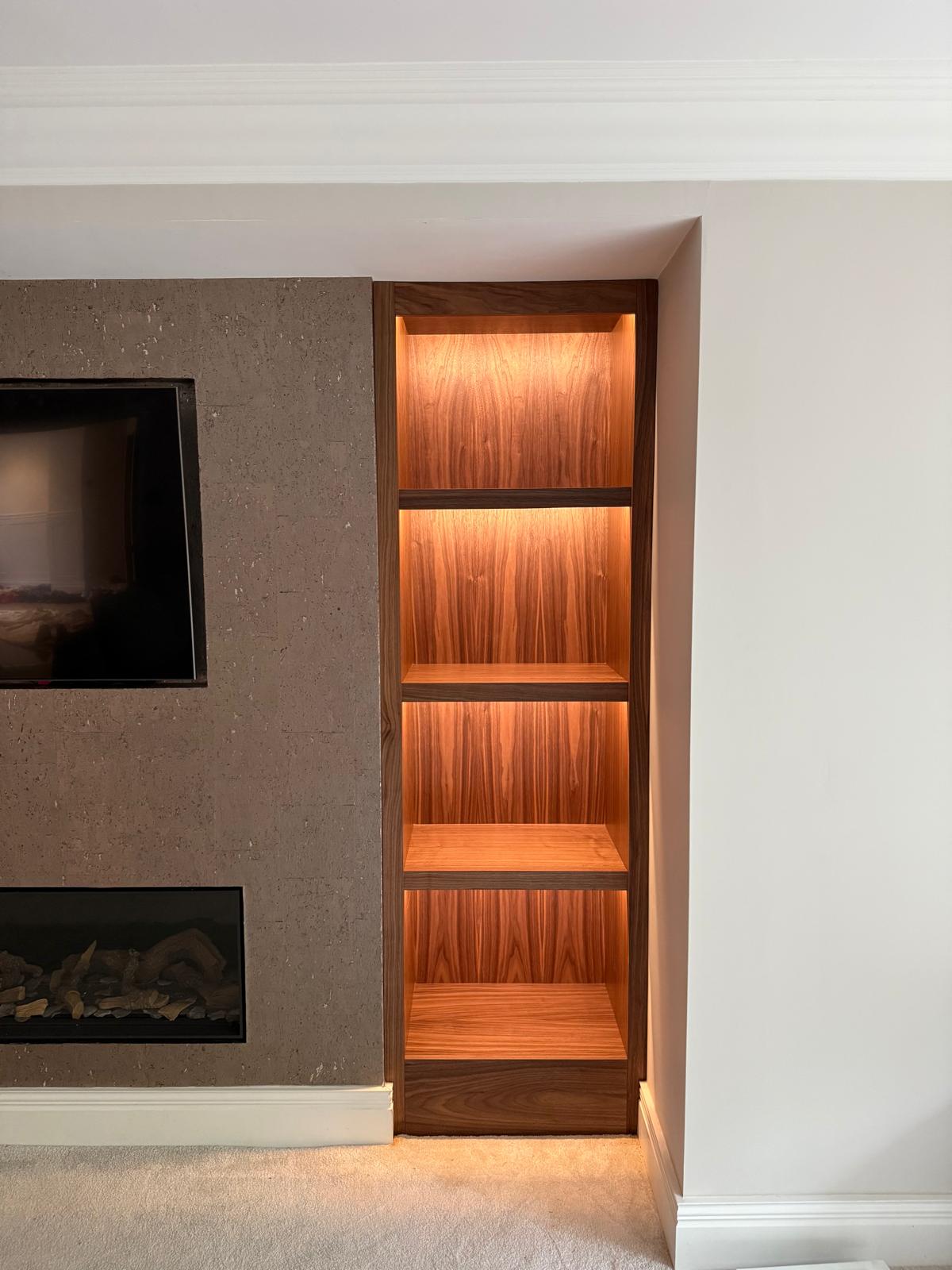 Detail of LED-lit walnut alcove shelving beside a stone-effect fireplace and television panel