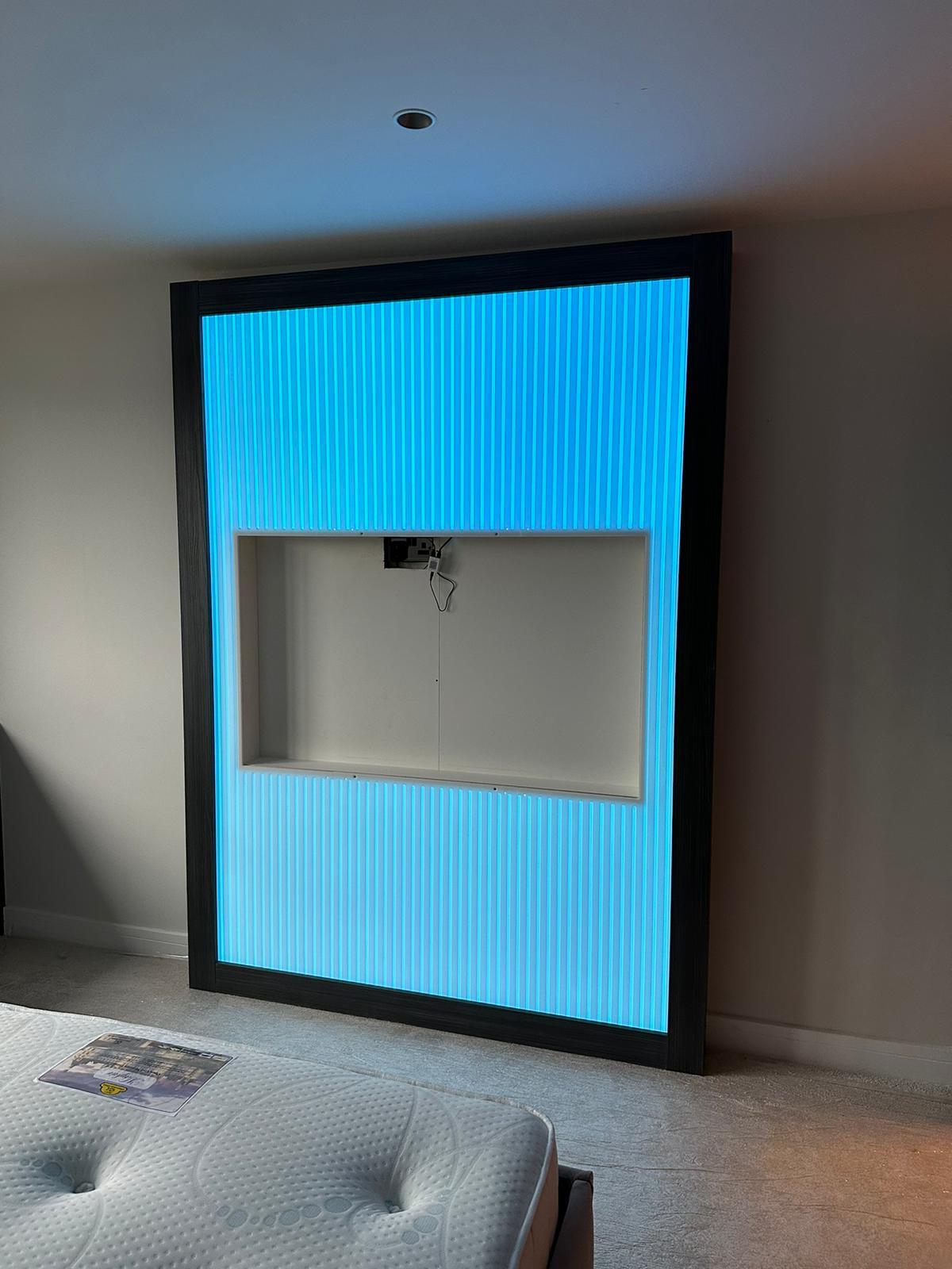 Dark framed fluted media wall with colour-changing LED backlighting and a recessed television opening, fitted in a bedroom