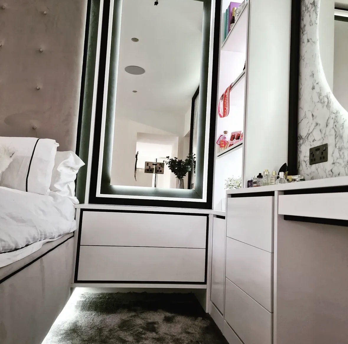 Detail of a backlit mirror above handleless fitted drawers with an illuminated display cabinet alongside