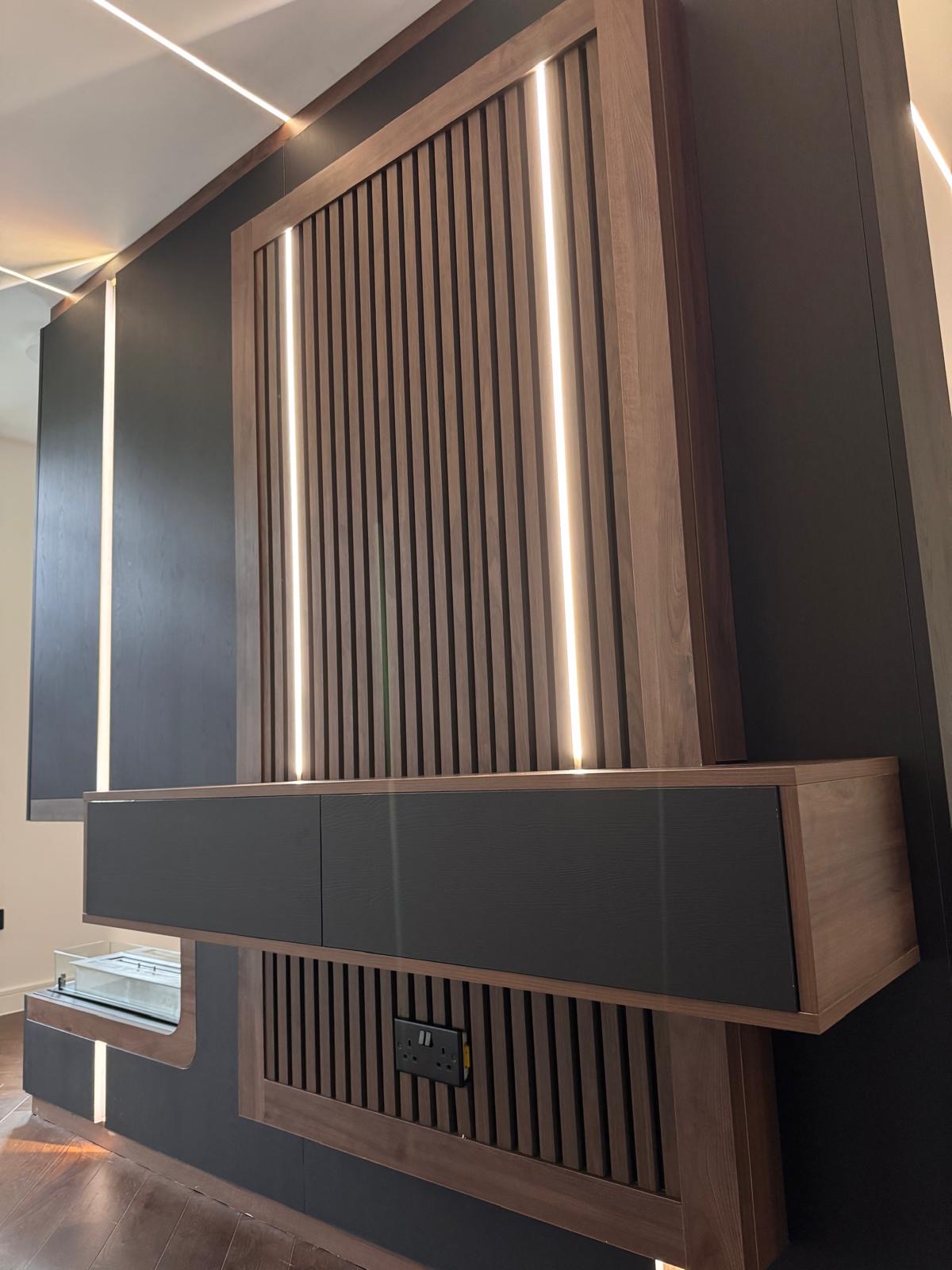 Detail of slatted walnut panelling with concealed LED strips above a floating black-fronted drawer unit on a bespoke media wall
