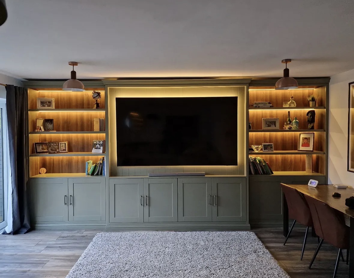 Sage green fitted media wall with lit walnut bookshelves flanking a recessed television