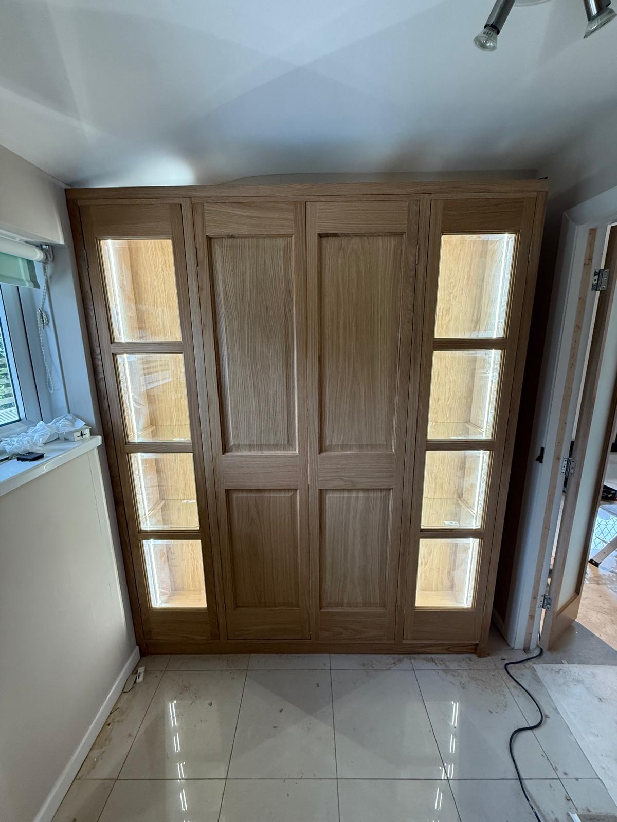 Oak display and storage unit with panelled centre doors and LED-lit glazed display cabinets either side, fitted into an alcove