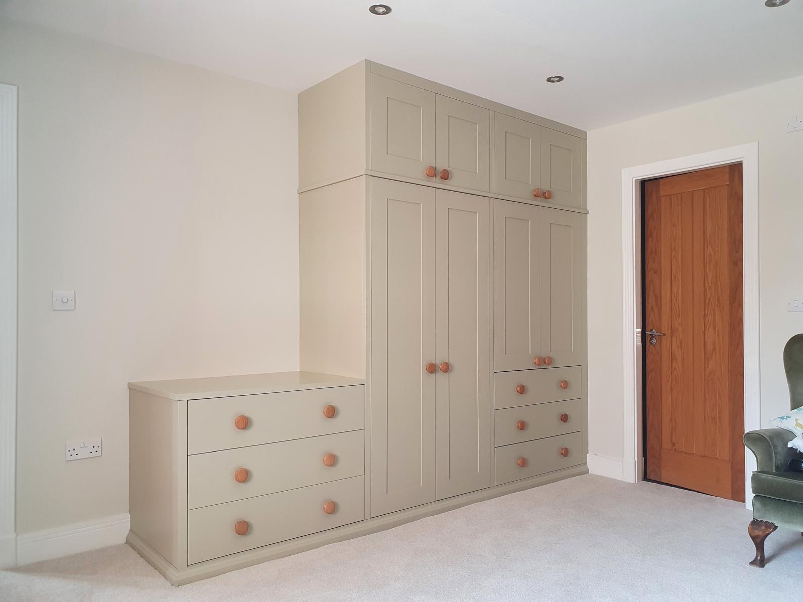 Stone-painted shaker wardrobes with top boxes, banks of drawers and a matching chest of drawers returning along the wall