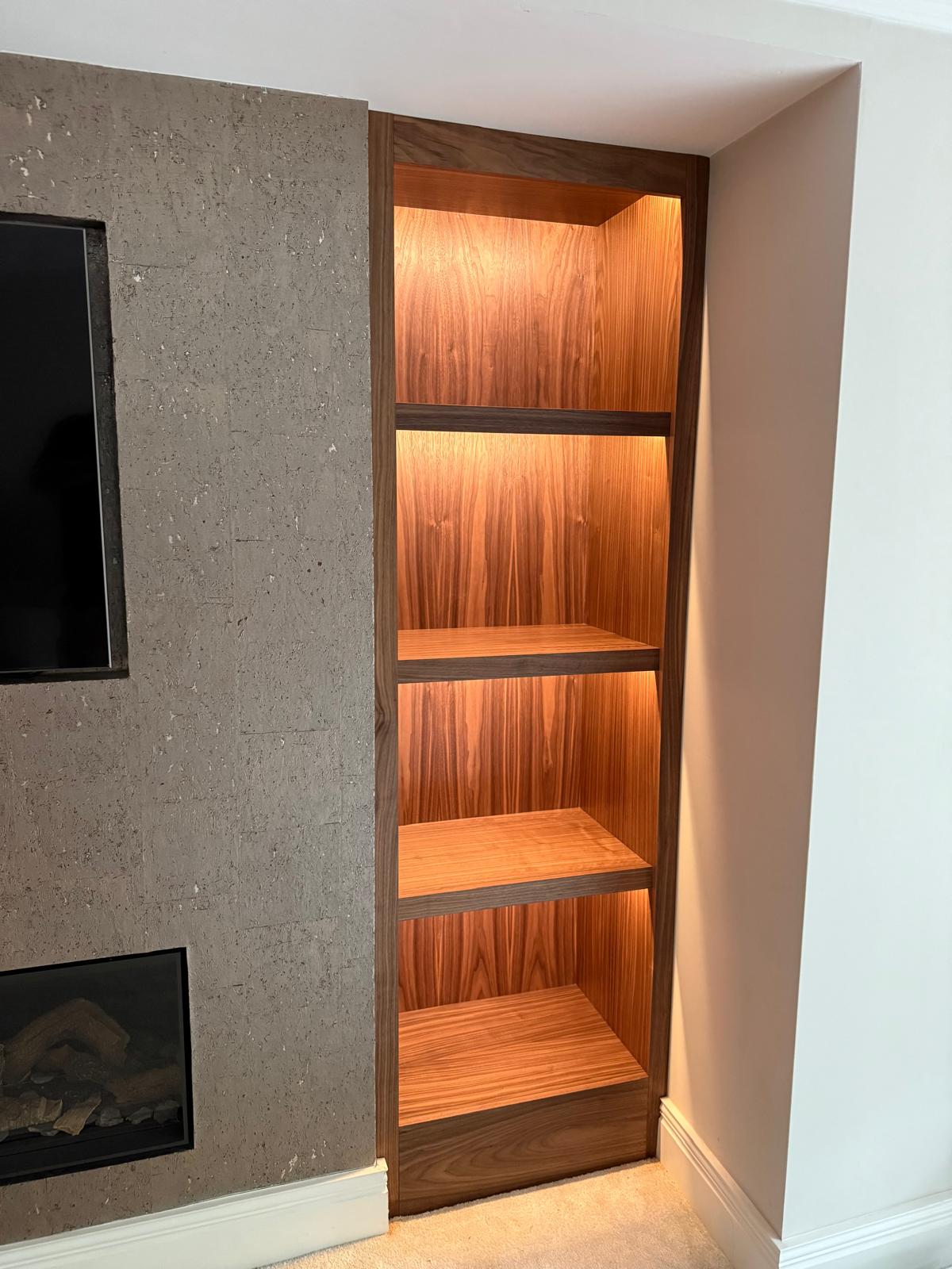 Tall LED-lit walnut alcove shelving with four open shelves, set alongside a stone-effect media wall