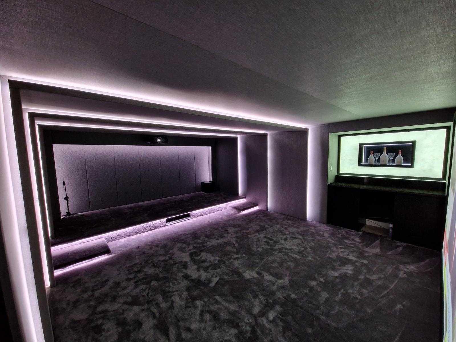 Home cinema room with fabric-panelled walls, layered cove LED lighting, projector and a fitted drinks bar to one side