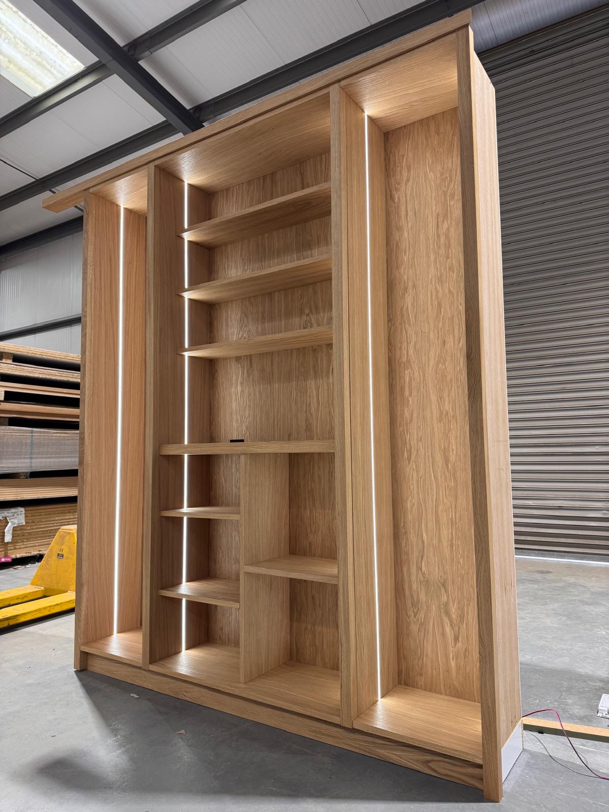 Freestanding oak bookcase with adjustable shelving and integrated vertical LED strips, photographed in the Chester Thomas workshop before delivery