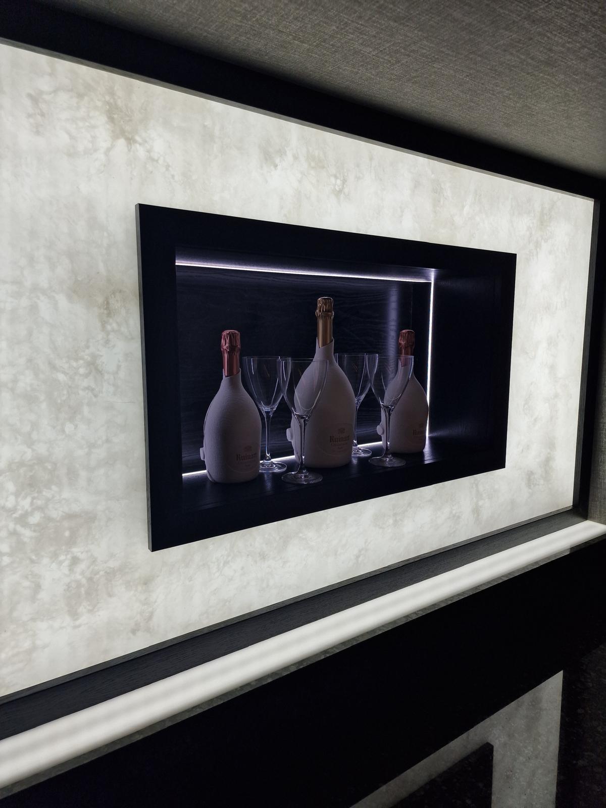 Close view of a framed display niche with concealed LED strip lighting holding champagne bottles and glasses