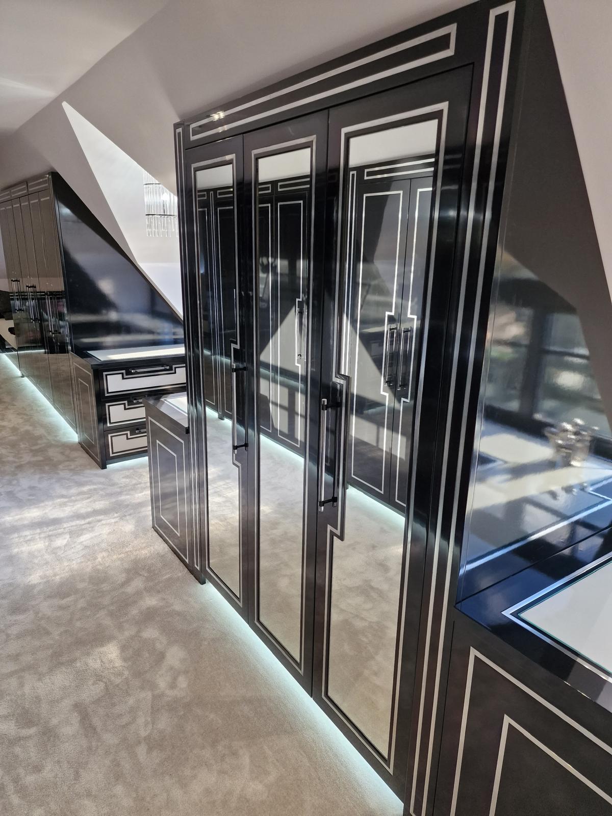 Gloss black wardrobe doors with mirrored panels and silver inlay framing, with a matching dressing table beyond