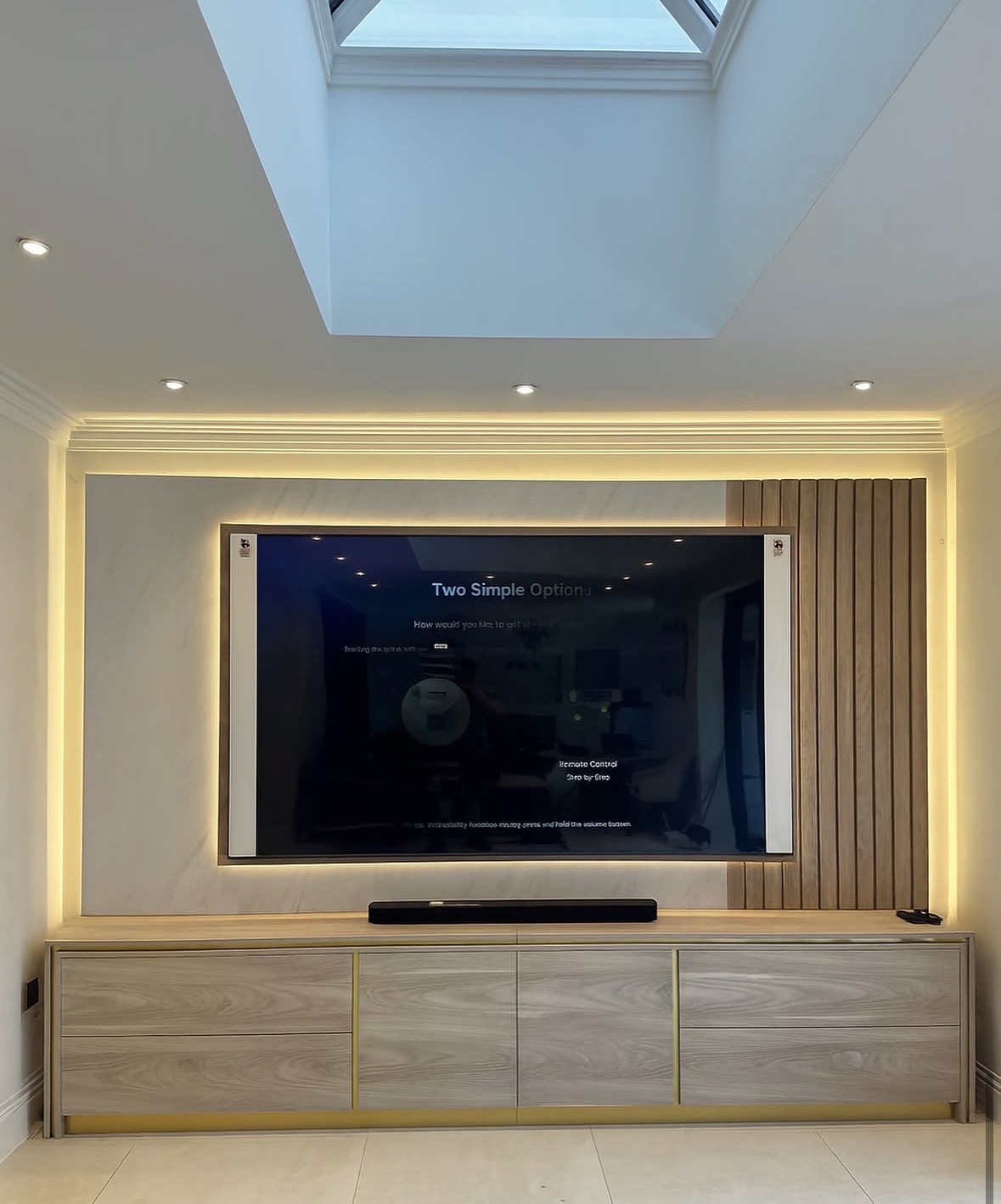 Bespoke media unit in pale ash with brass shadow lines, backlit television panel and oak slatted wall detail