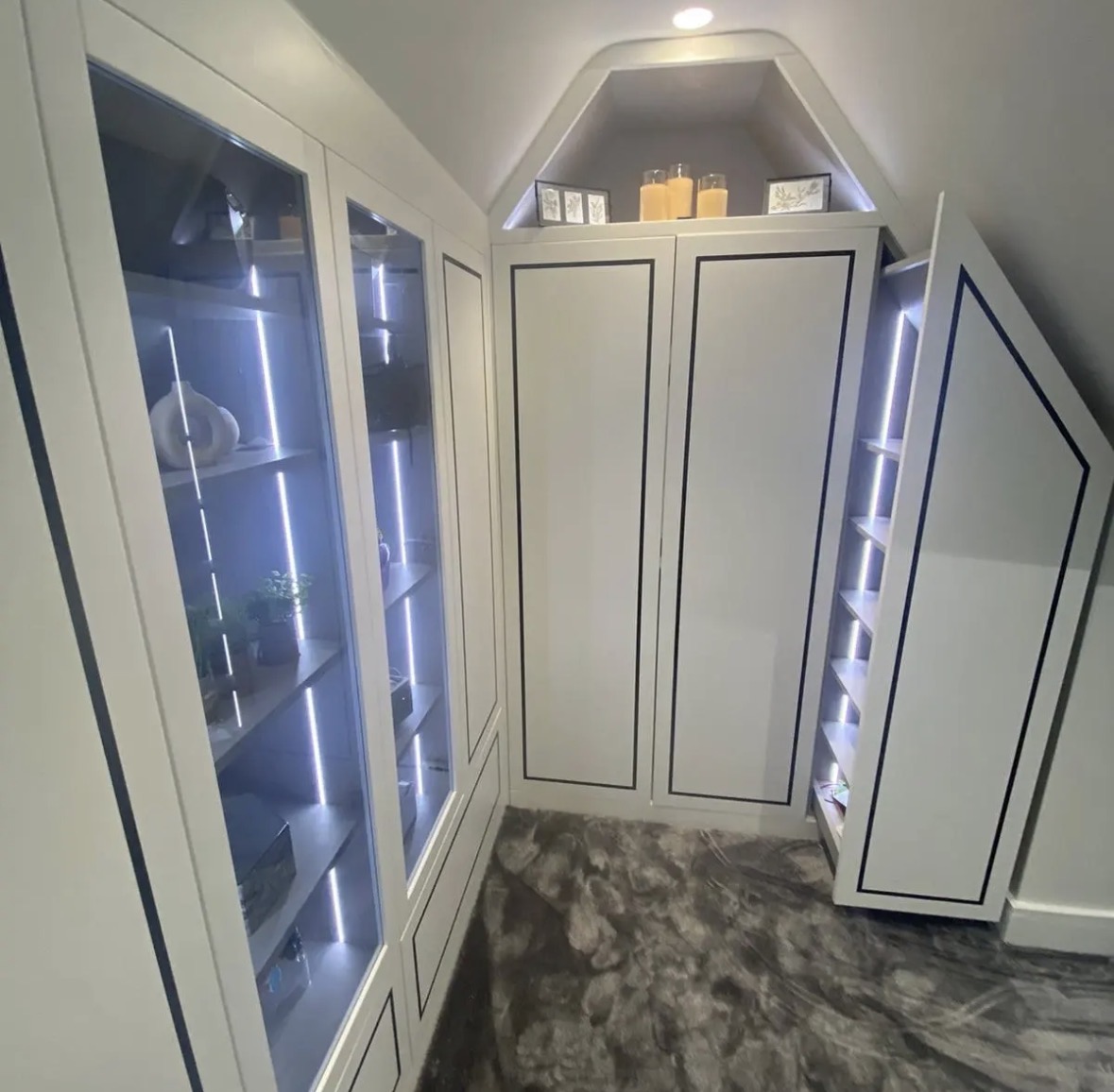 Loft dressing room with ivory wardrobes, glazed LED-lit display cabinets and shelving shaped to the sloping ceiling