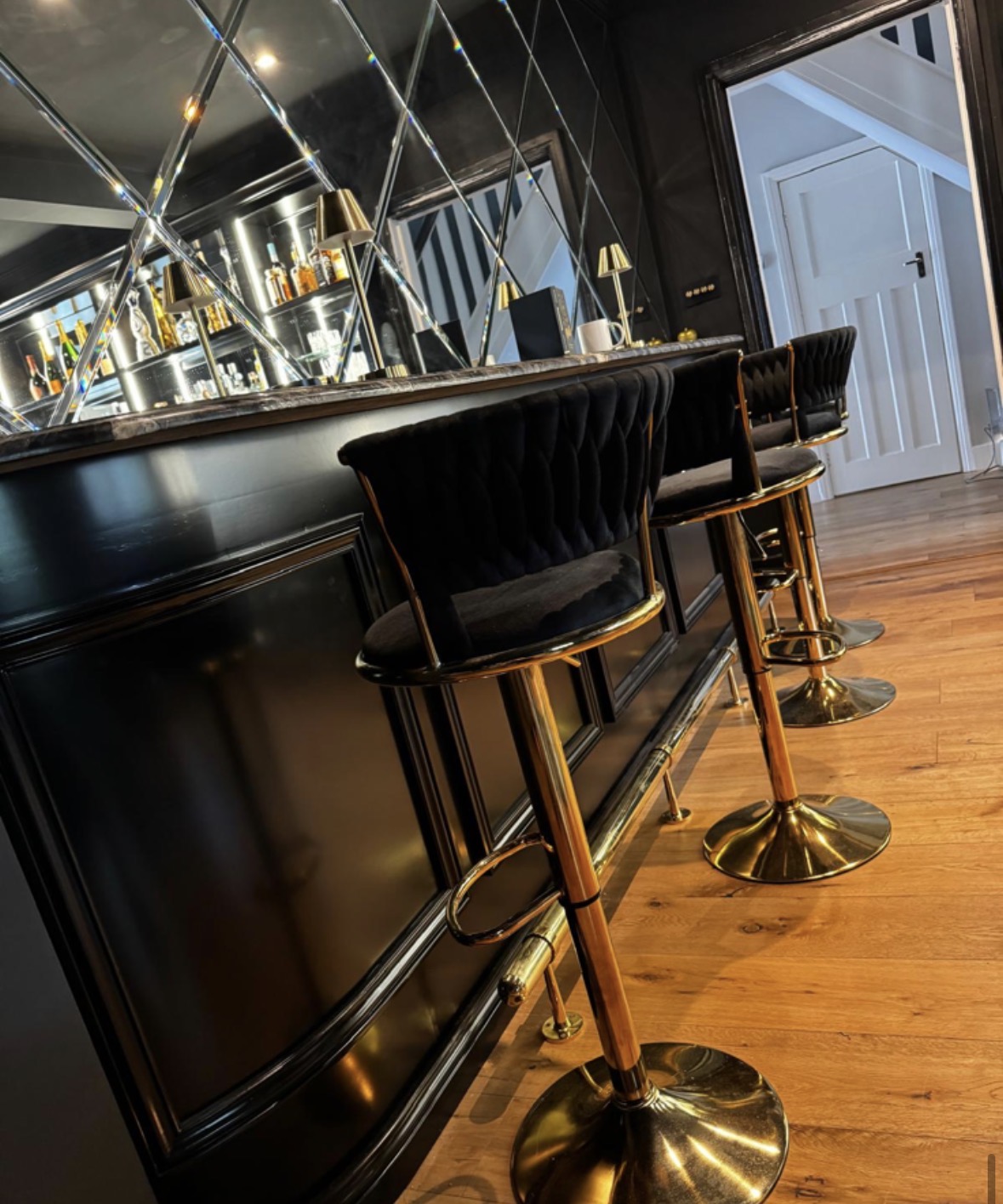 Curved black bar with brushed gold and black leather stools set against antique mirrored panelling