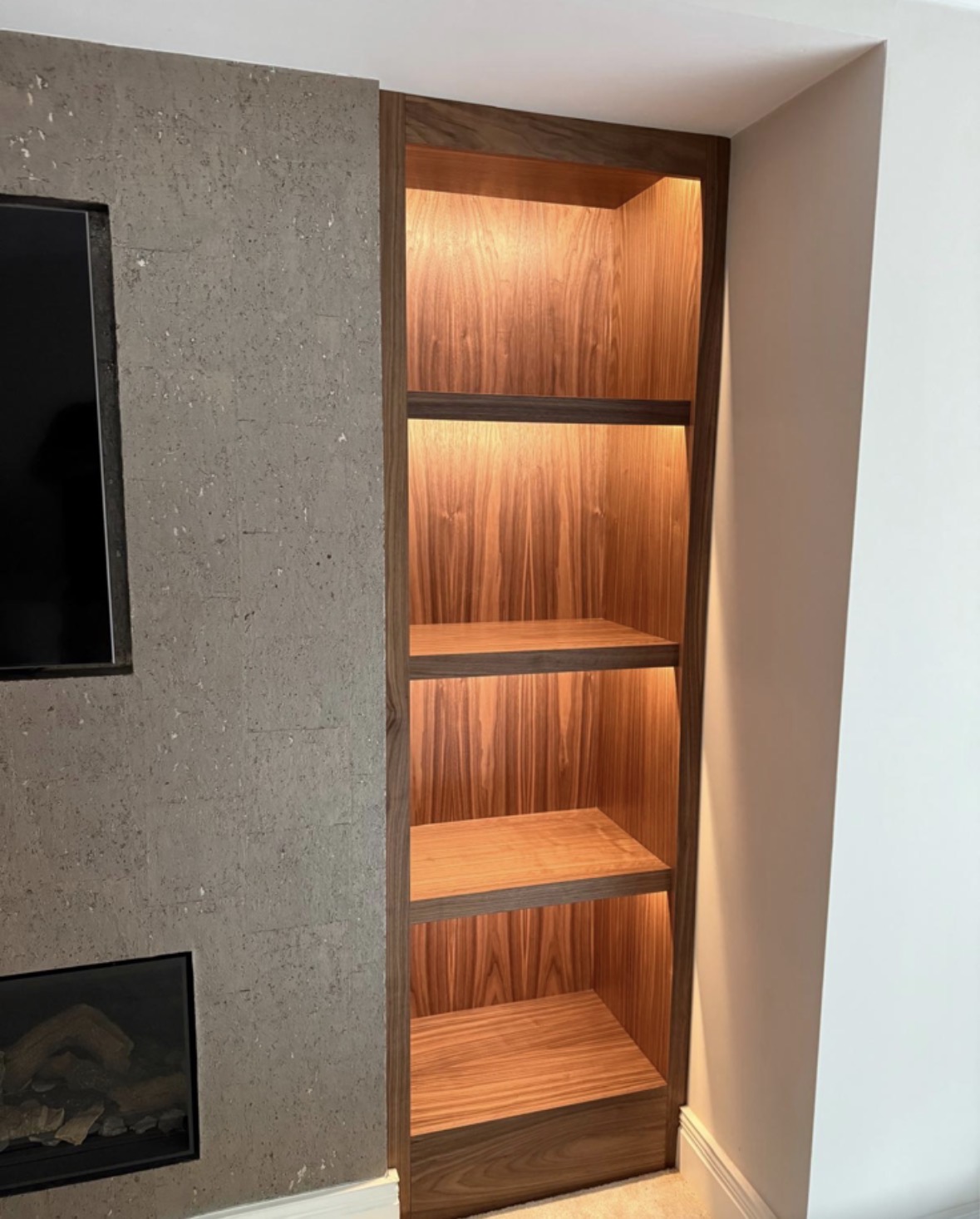 Detail of an LED-lit walnut bookcase with figured grain shelving set beside the stone-clad panel of a bespoke media wall