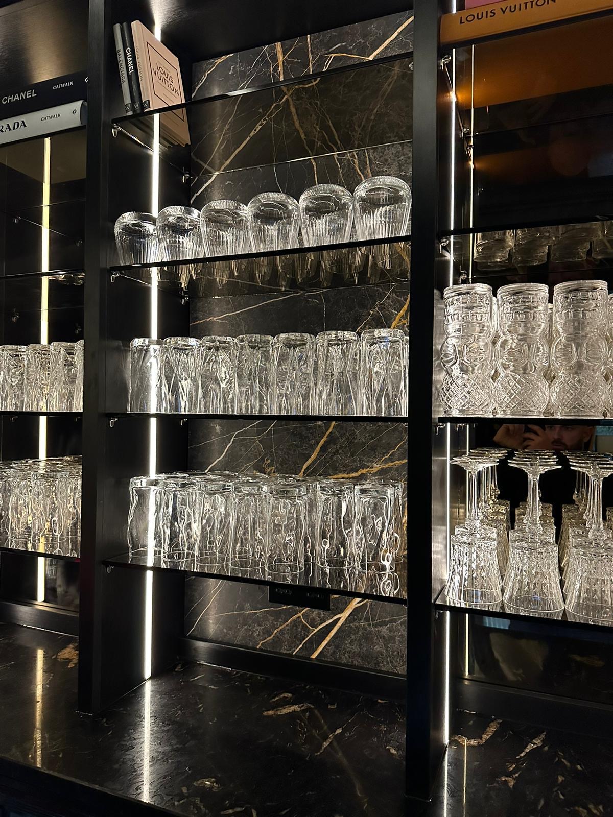 Close view of lit glass shelves against black marble with cut crystal tumblers and decanters