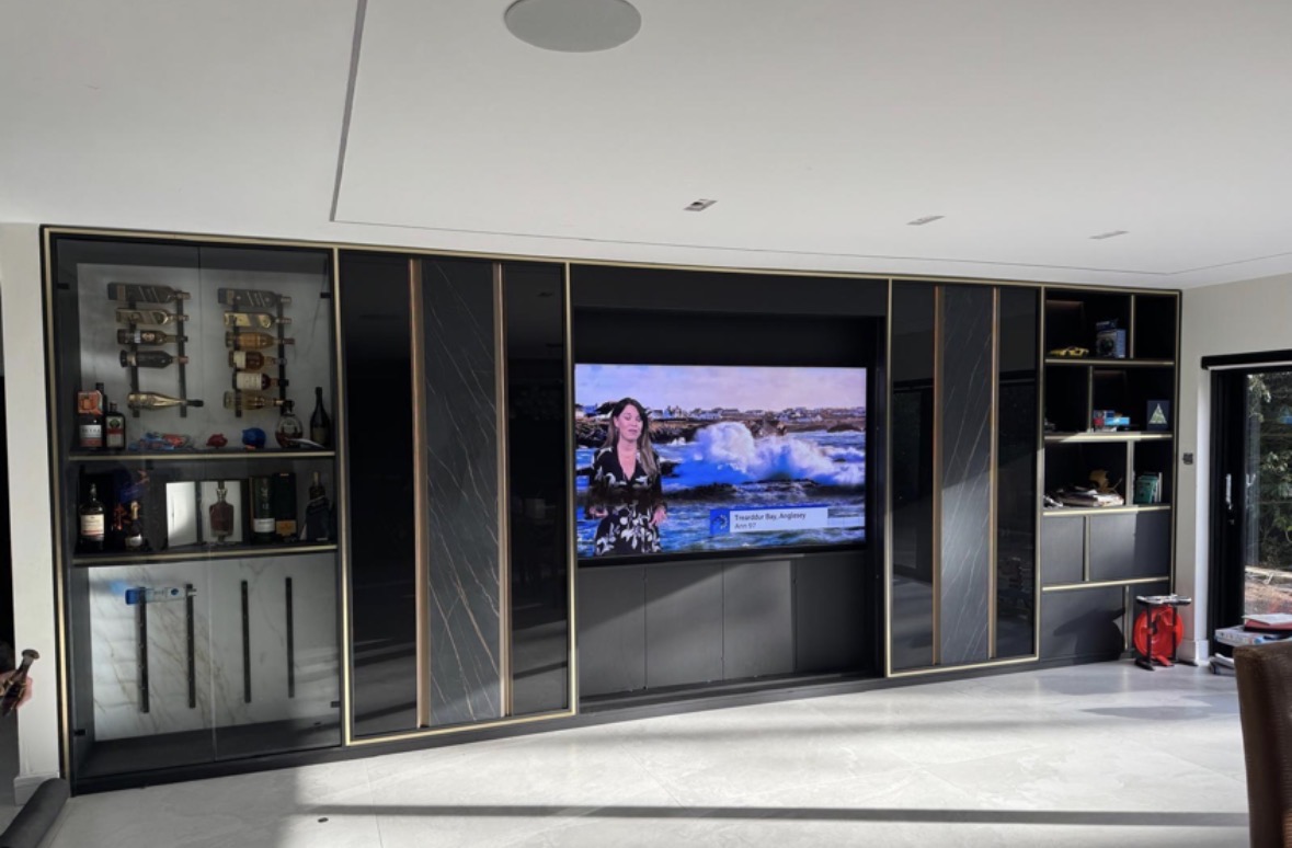 Wide media wall in dark cabinetry with fluted feature panels, a recessed television and lit display shelving either side