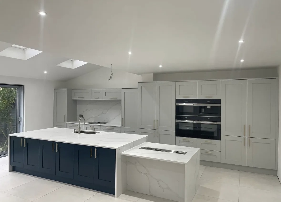 Hand-painted shaker kitchen with a navy island, marble-effect worktops and tall pale grey cabinetry housing built-in ovens