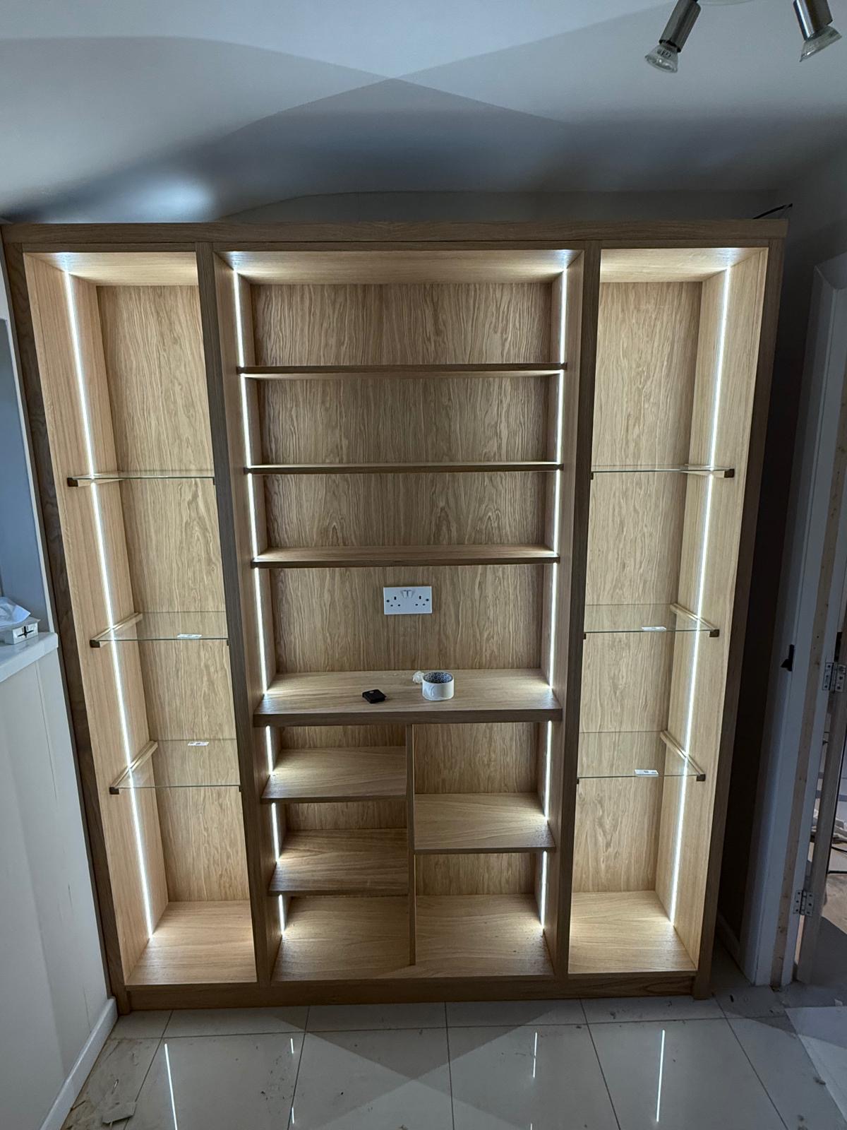 Oak display unit with LED-lit open shelving, glass shelves either side and a central shelf run with a socket built in