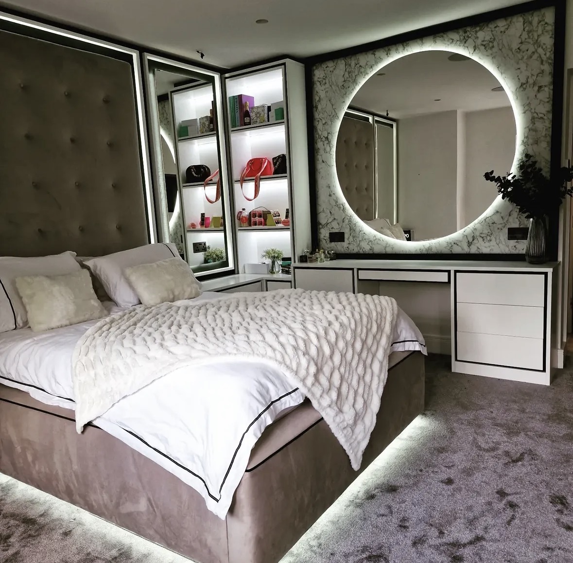 Bespoke bedroom and dressing suite combining an upholstered headboard wall, lit display shelving and a fitted dressing table
