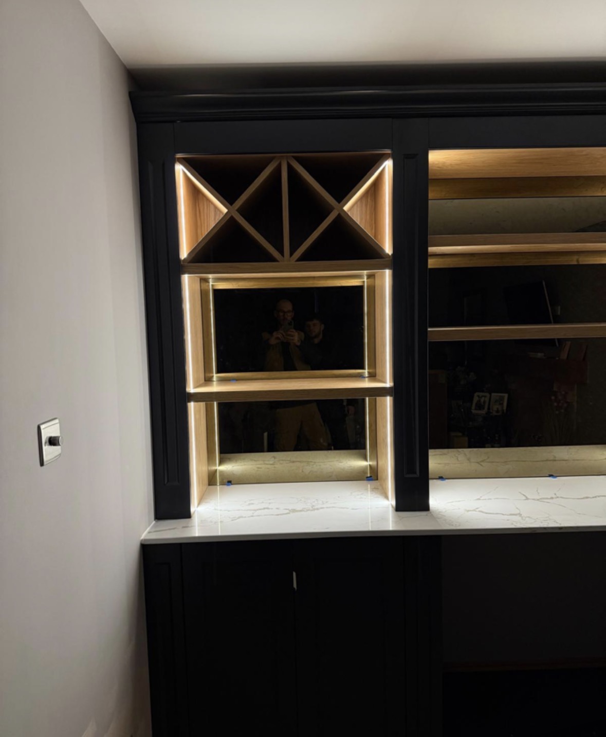 Detail of LED-lit oak cross-hatch wine racking and antique mirrored shelving within a navy painted drinks unit