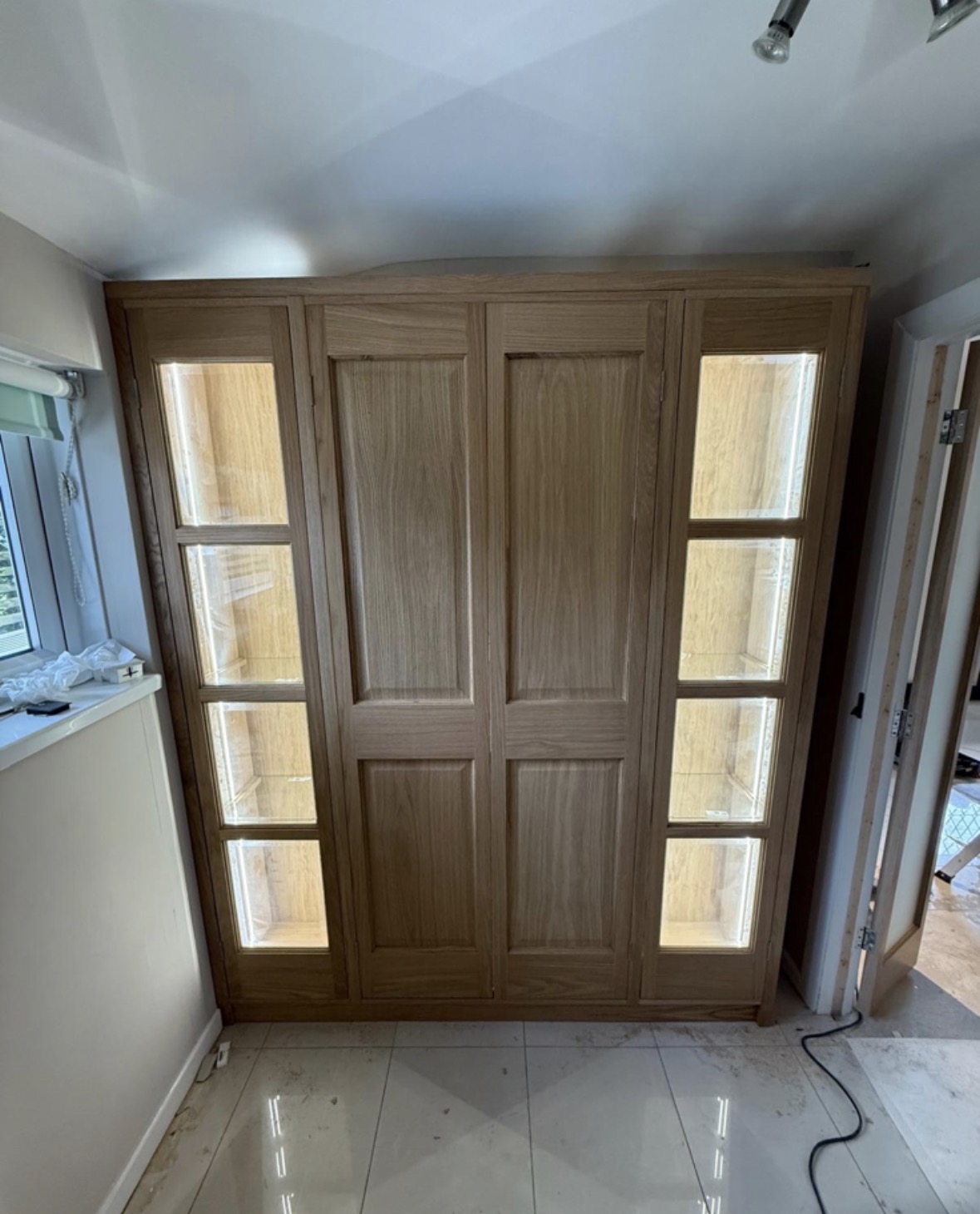 Fitted oak cabinet with two panelled centre doors flanked by LED-lit glass display shelving, built into an alcove