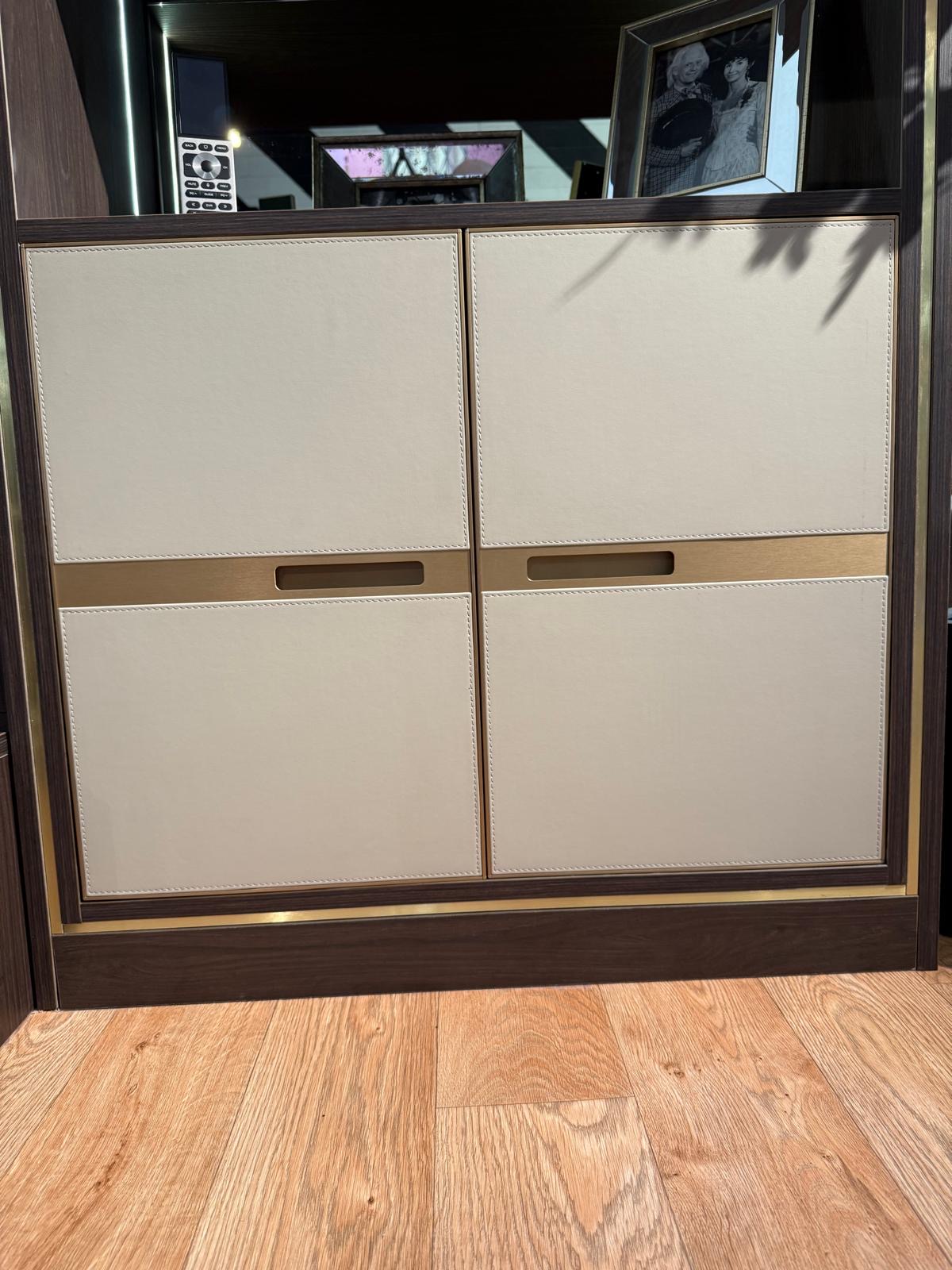 Close detail of cream stitched-leather cabinet doors with brushed brass recessed handles in a dark oak framed cabinet