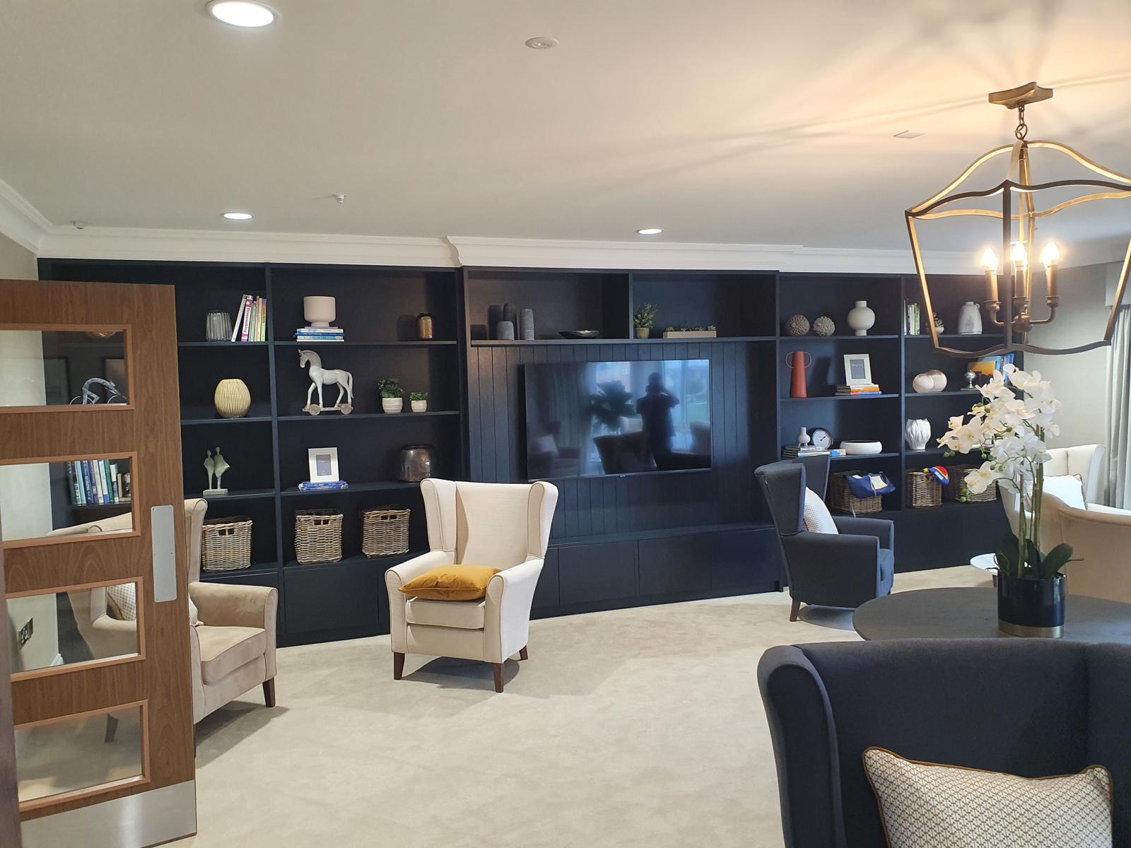 Wall-to-wall navy media wall in a lounge with open bookcase shelving either side of a panelled television recess and closed base cupboards