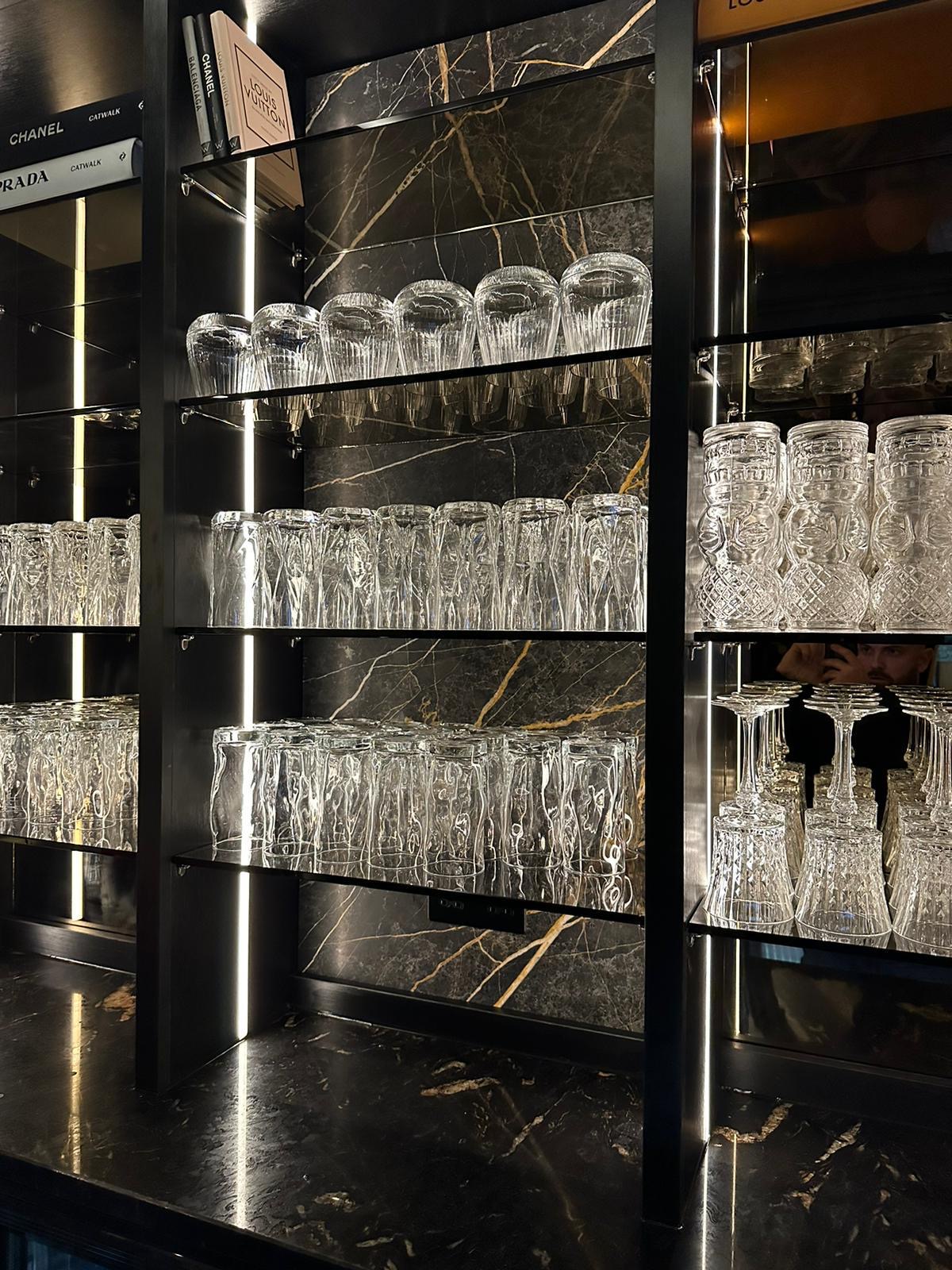 LED-lit glass display shelving set against a black marble back panel, holding cut crystal glassware