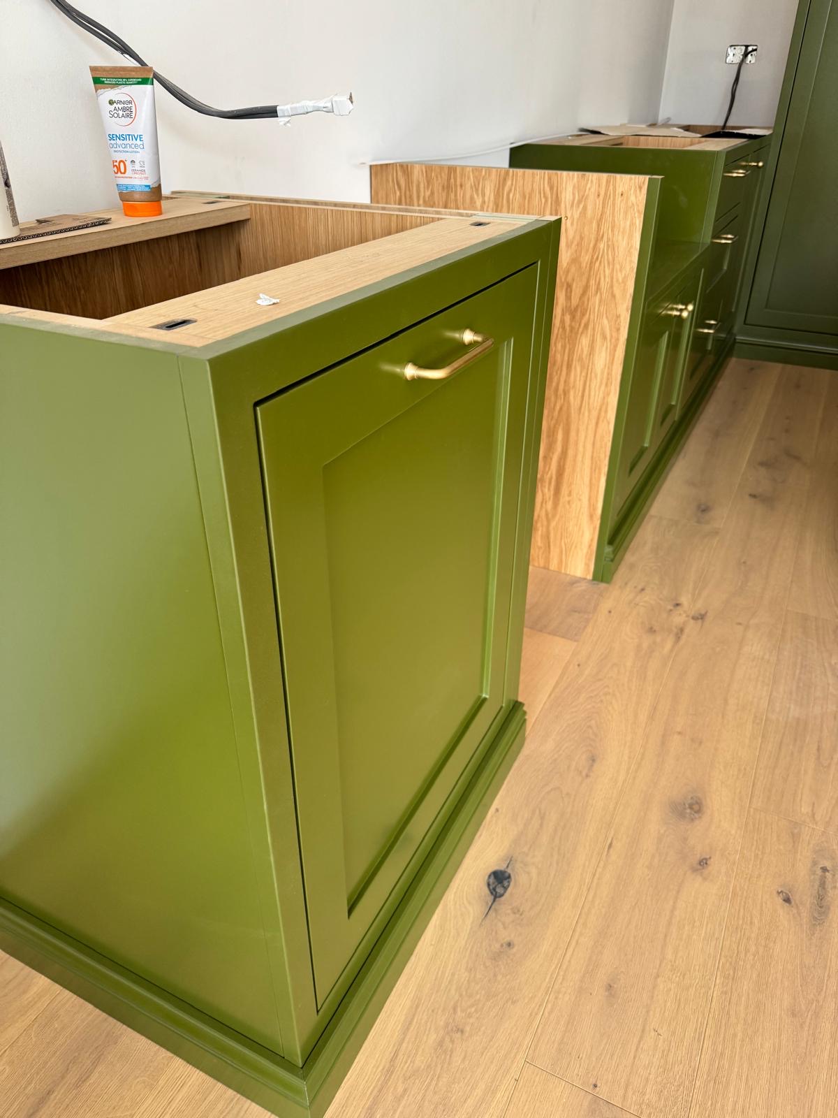 Olive green painted cabinetry with an oak-framed run behind, photographed part-way through a bespoke kitchen installation