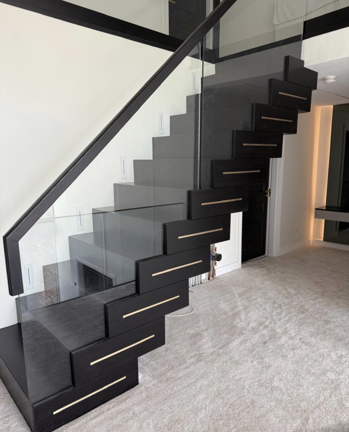 Dark timber staircase with LED-lit treads, a glass balustrade and fitted storage built into the space beneath