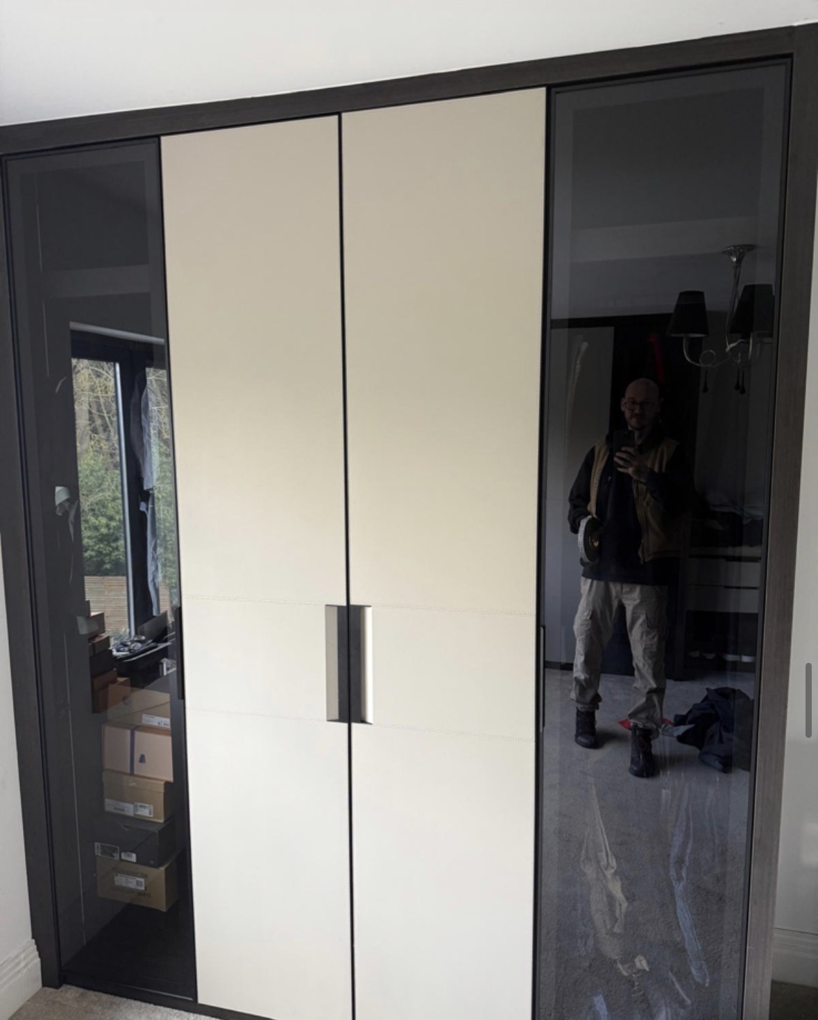 Tall fitted wardrobe with cream centre doors and smoked glass hinged doors either side, framed in dark metal