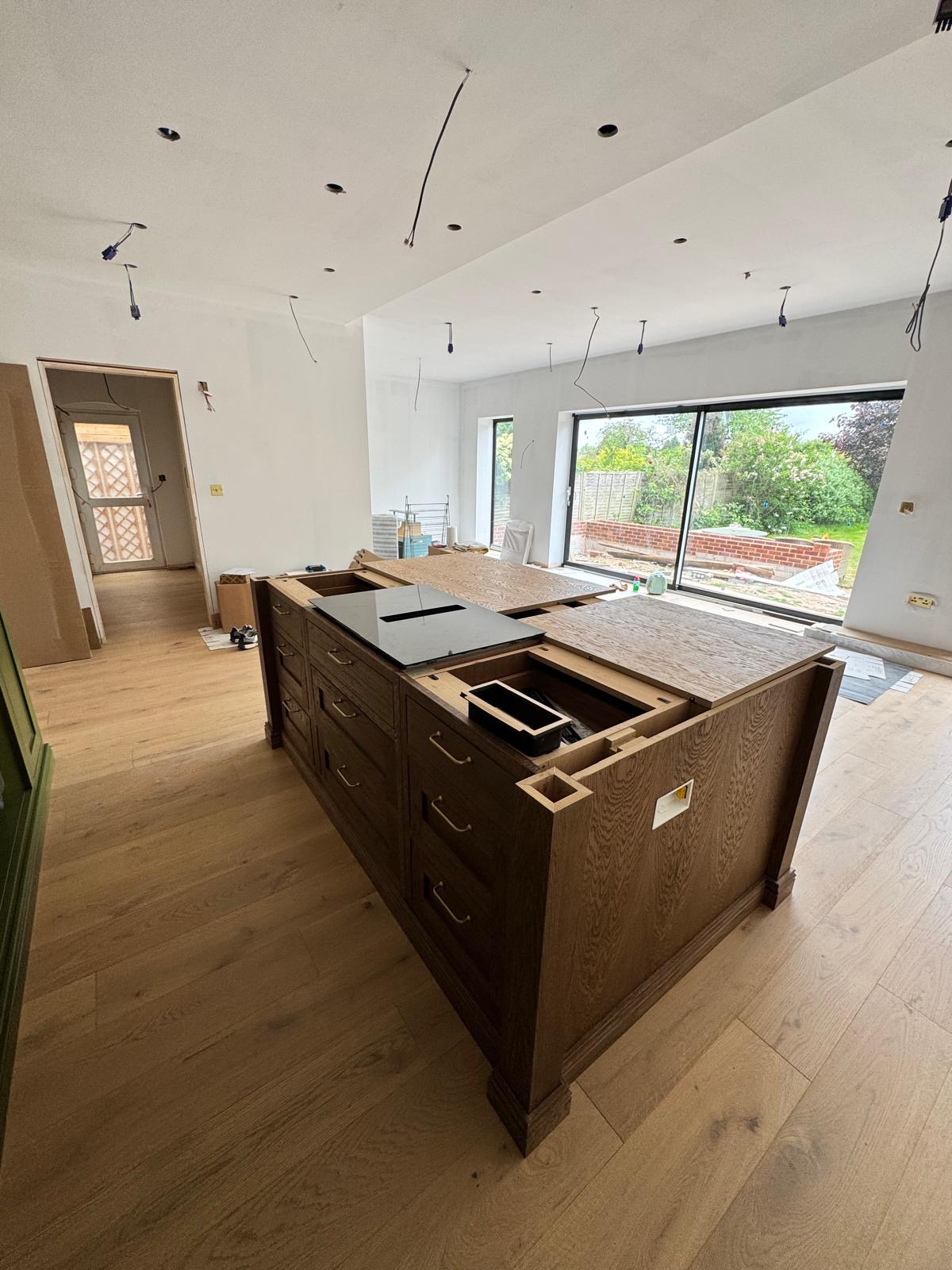 Bespoke dark oak kitchen island with brass bar handles during installation, prepared for worktops and a flush hob